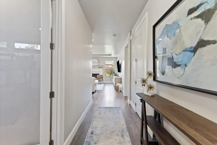 Wood-finish flooring extending through the hallway, white interior doors, and recessed lighting in the background