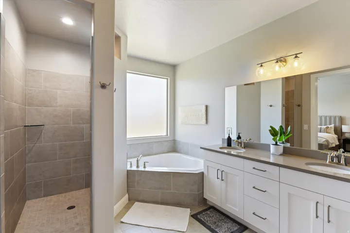 Dual vanity with undermount sinks, corner soaking tub, walk-in shower with tiled walls, and frosted window