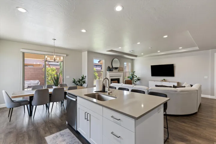 Open-concept living space featuring wood-finish flooring, recessed lighting, a kitchen island with a built-in sink, a dining area with a glass sliding door, and a living area with a fireplace