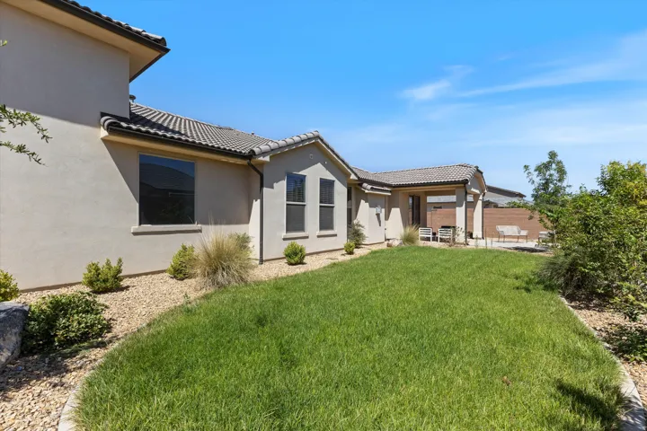Stucco exterior with a tiled roof, featuring a covered patio, a grass lawn, and a gravel perimeter
