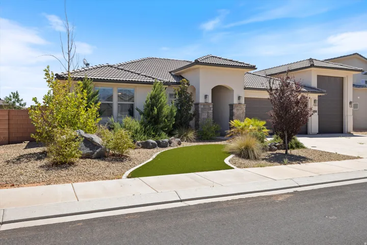 Stucco exterior with stone accents, tiled roofing, an arched entry, and a gravel and artificial turf landscaping