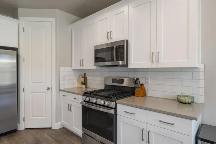 White shaker cabinetry, stainless steel appliances, solid surface countertops, subway tile backsplash, and wood-finish flooring
