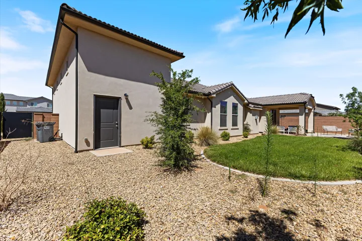Backyard featuring a stucco exterior, tiled roof, rock landscaping, and a manicured lawn area