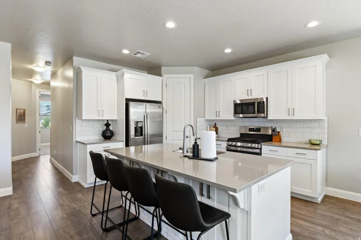 Kitchen featuring an island with counter seating, stainless steel appliances, white cabinetry, a subway tile backsplash, and wood-finish flooring