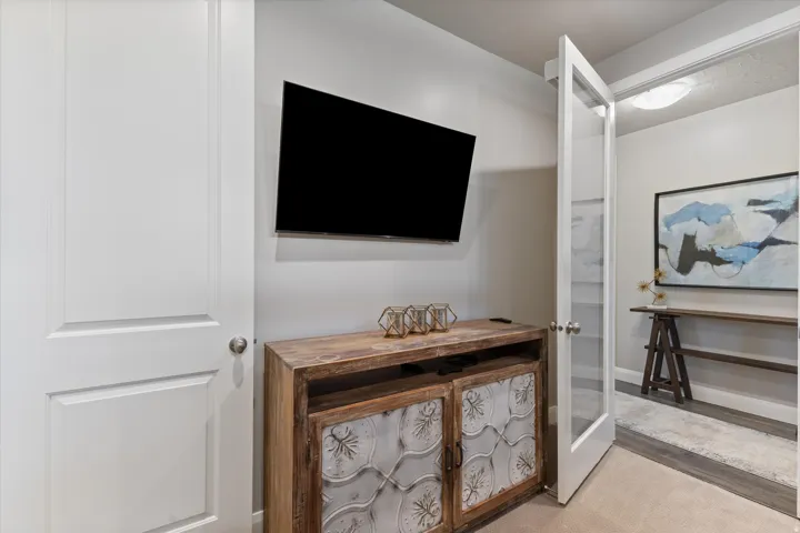Built-in wall-mounted television, wood-finish console with decorative metal panels, and a glass-paneled interior door