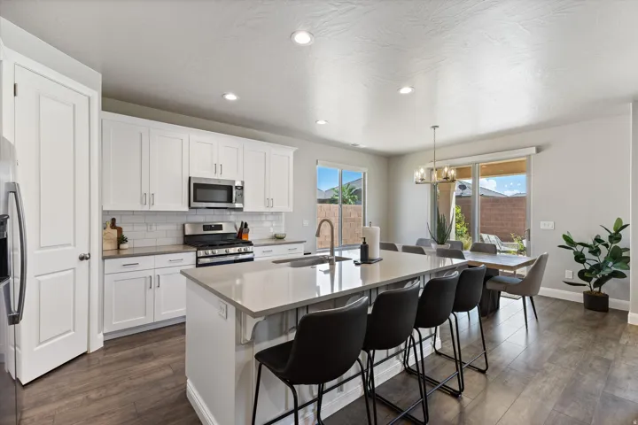 Kitchen featuring white shaker cabinetry, stainless steel appliances, a center island with countertop seating, a subway tile backsplash, and wood-finish flooring