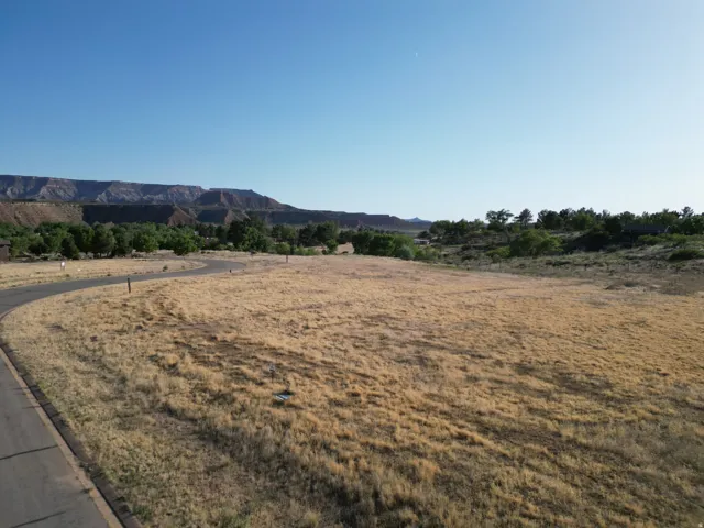 Expansive open land with natural grasses, paved road frontage, and distant mesa formations
