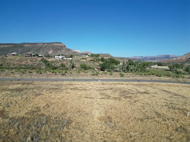 Expansive undeveloped land with a paved road frontage, surrounded by distant mountains and a clear sky