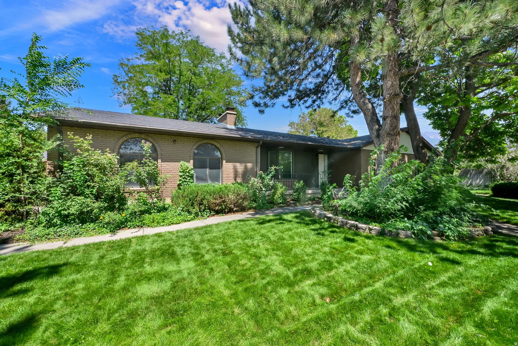 Brick exterior with arched windows, mature landscaping, and a manicured front lawn