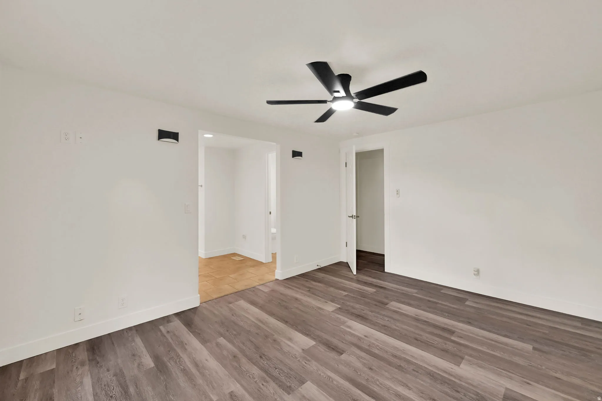 Wood-finish flooring with white baseboards, a ceiling fan with integrated lighting, and two wall-mounted sconces