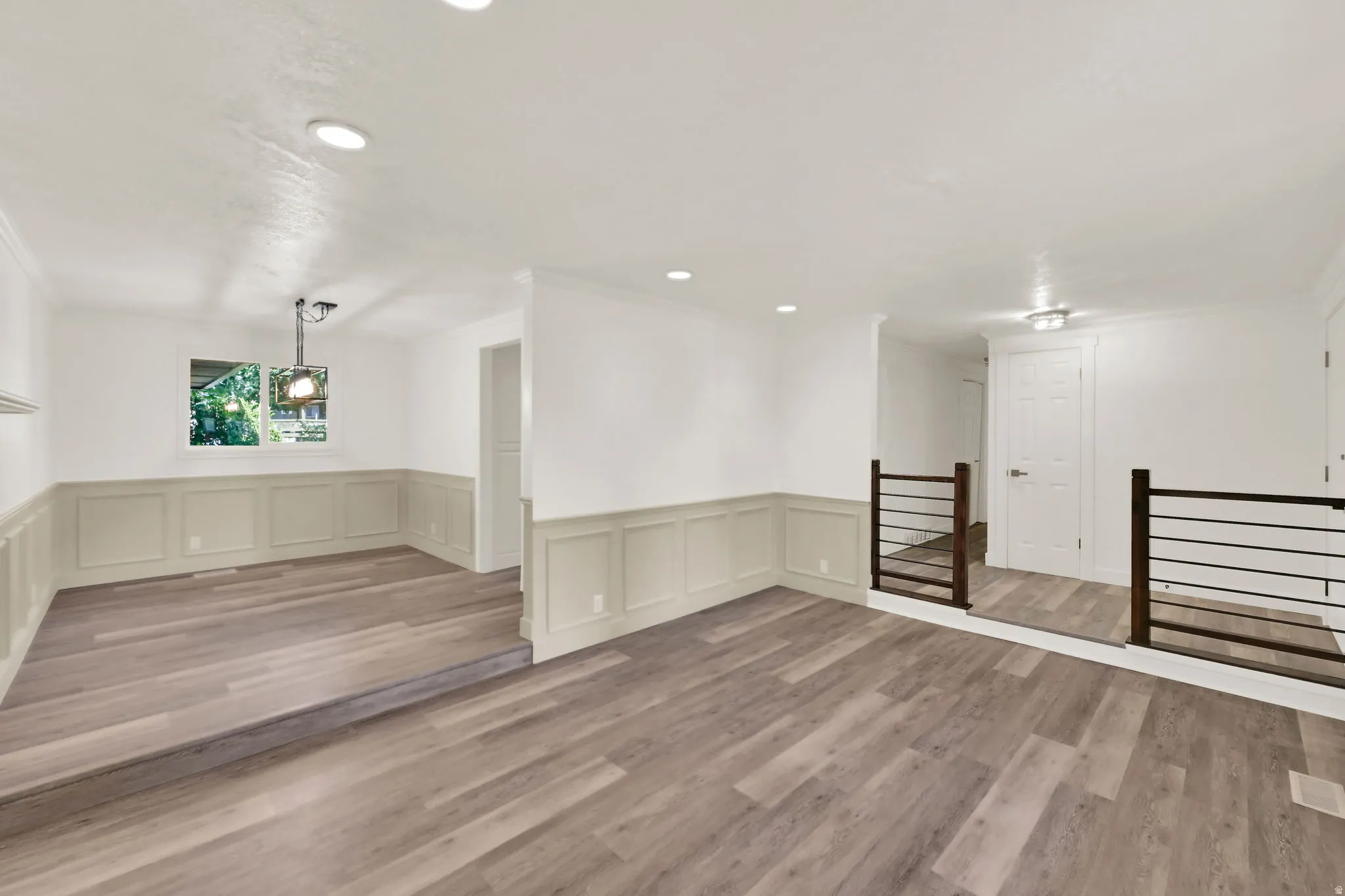 Wood-finish flooring throughout, wainscoting detail, recessed lighting, and a modern horizontal bar railing system