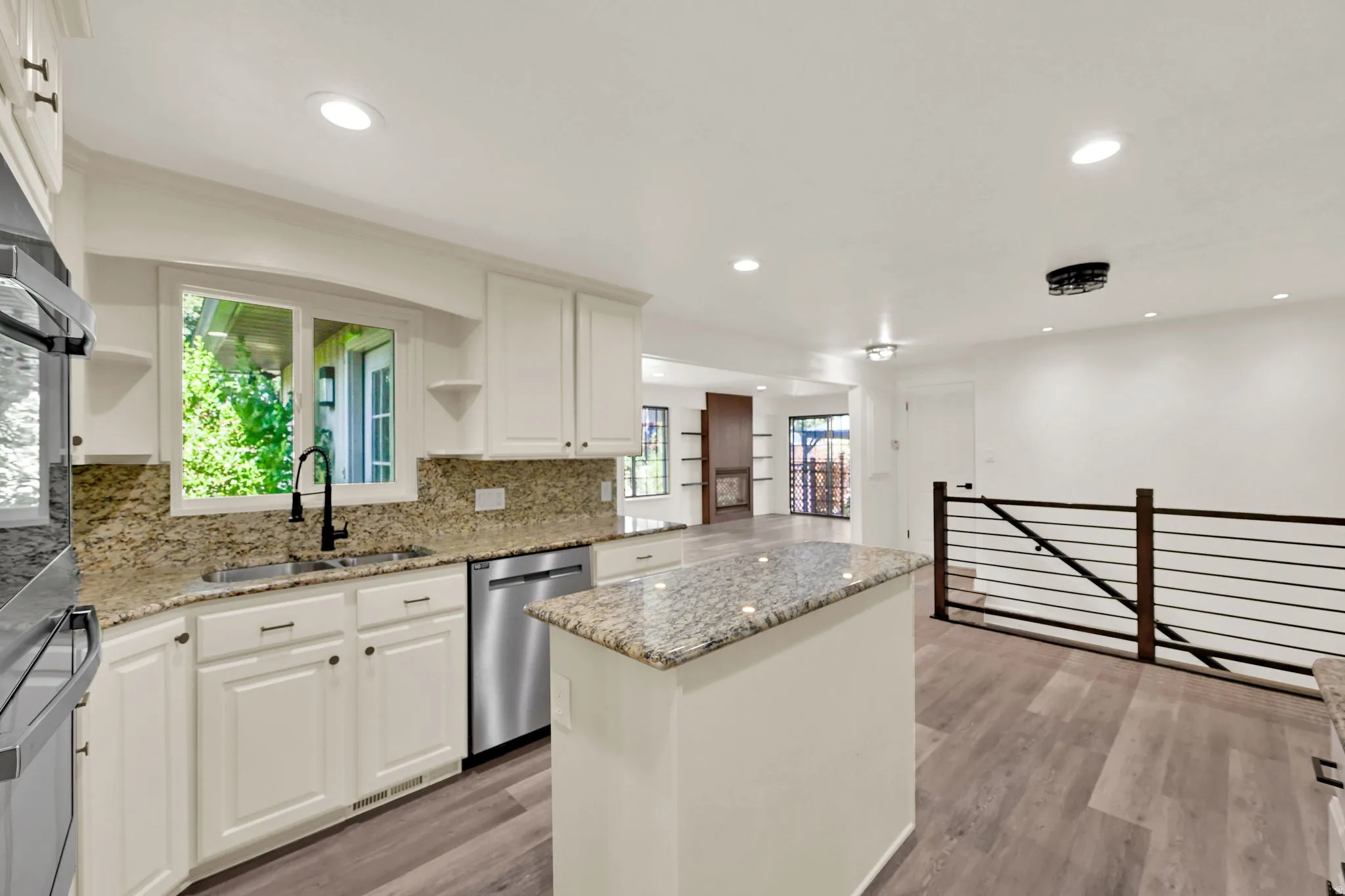 White cabinetry with granite countertops, stainless steel appliances, wood-finish flooring, recessed lighting, and a contemporary railing system