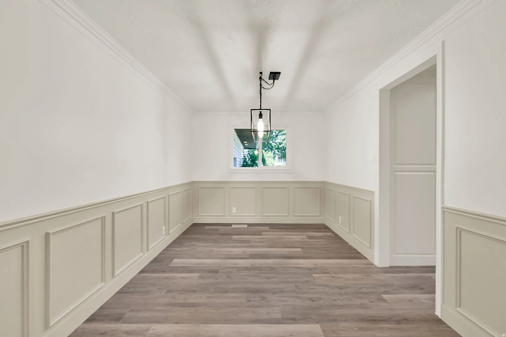 Wood-finish flooring, wainscoting, crown molding, and a modern pendant light fixture