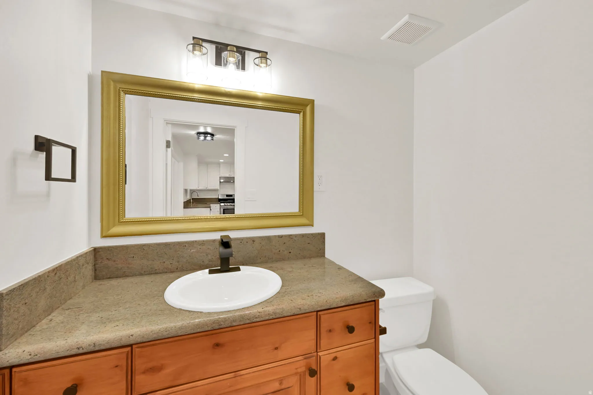 Wood-finish vanity with a drop-in sink, stone countertop, and bronze-finish faucet