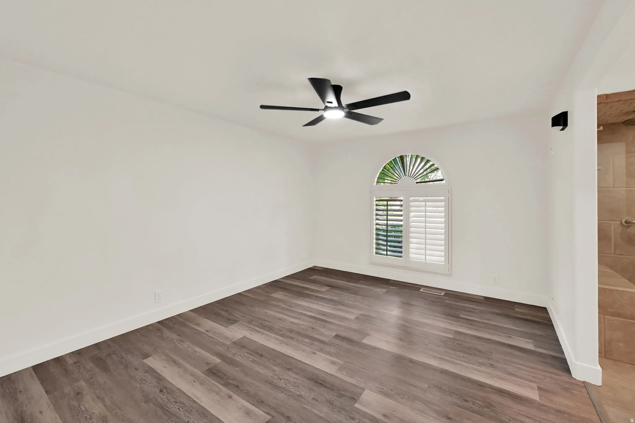 Wood-finish flooring, contemporary ceiling fan, arched window with plantation shutters, recessed lighting, and white walls
