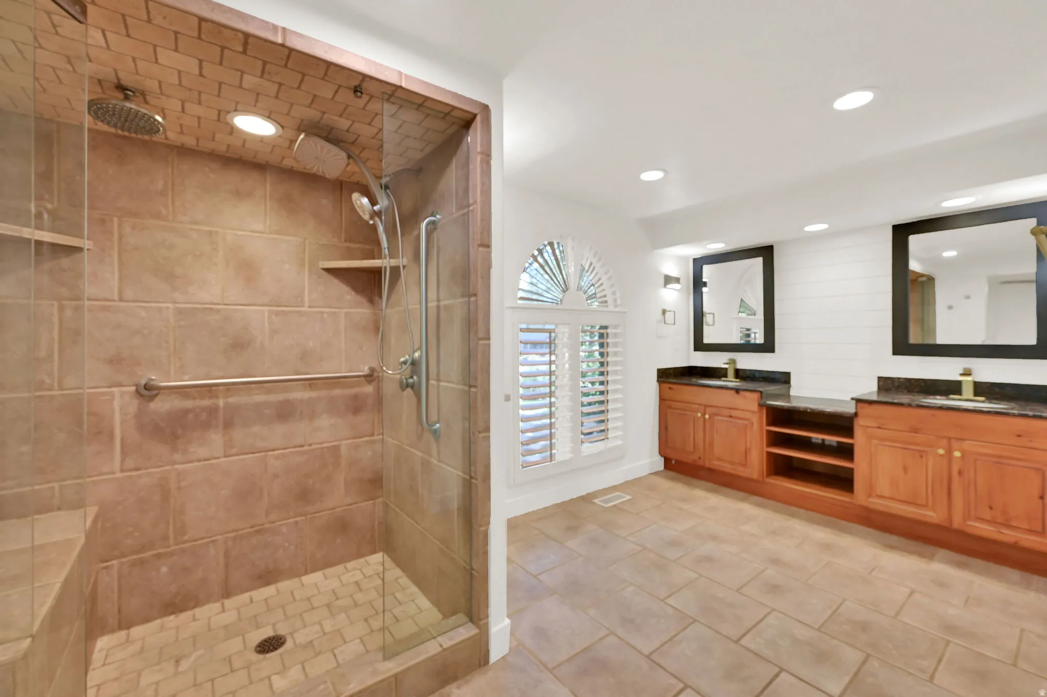 Spa-inspired primary bathroom featuring a spacious walk-in shower with travertine tile surround, rainfall showerhead, and built-in shelving