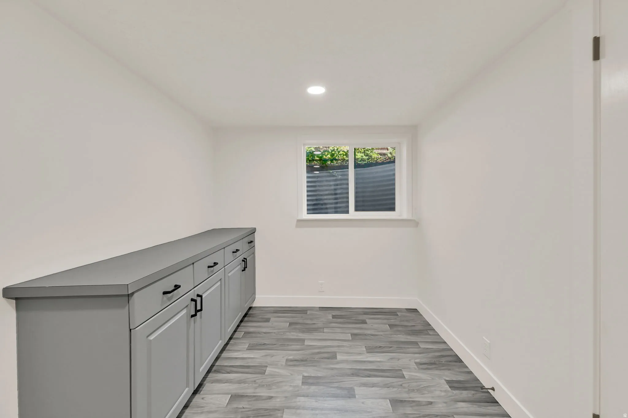 Recessed lighting, wood-finish flooring, built-in cabinetry with matte black hardware, solid surface countertop, and a window with white trim
