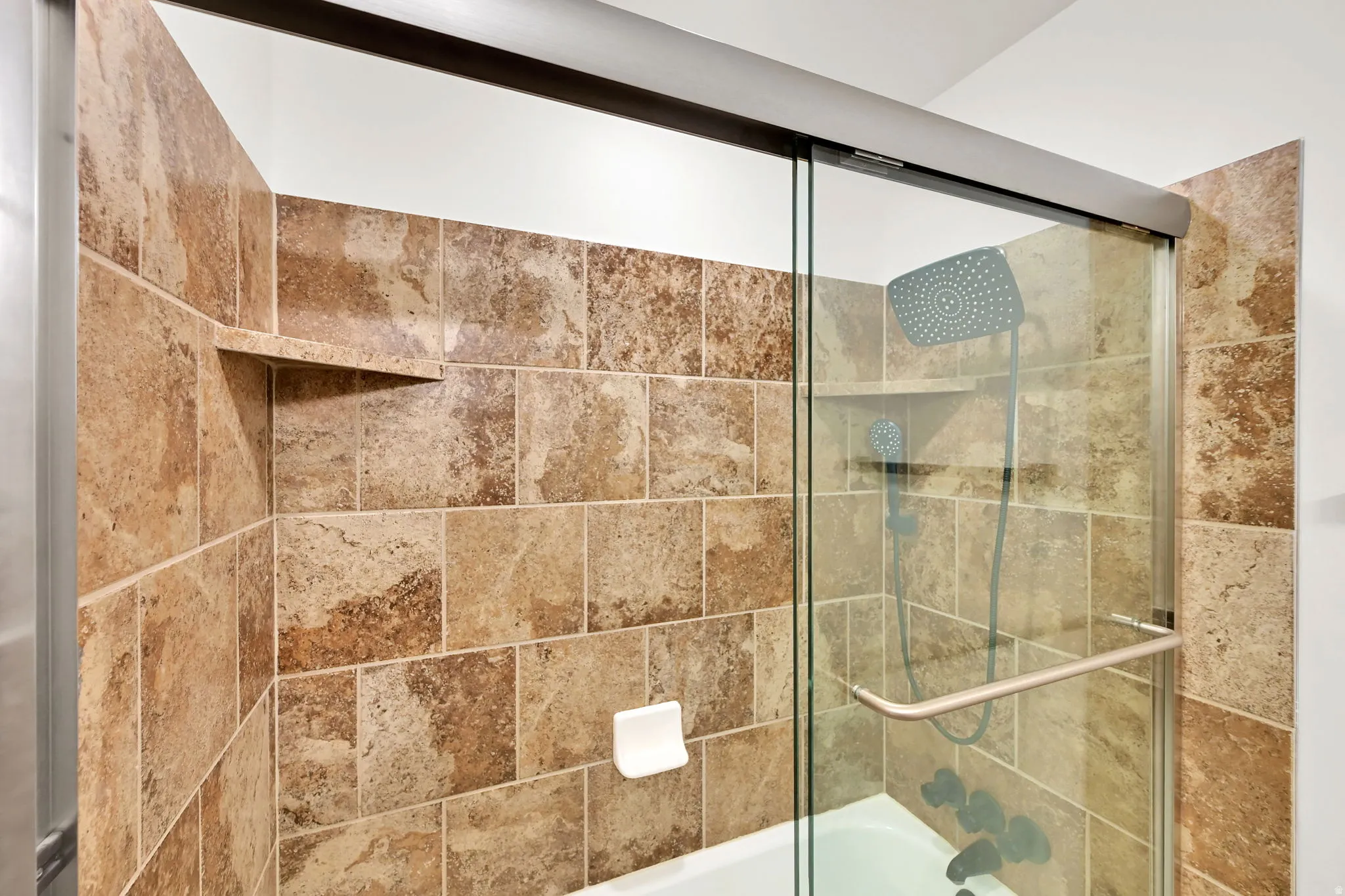 Full shower enclosure featuring a sliding glass door, mosaic tile surround, built-in shelving, and a rain showerhead