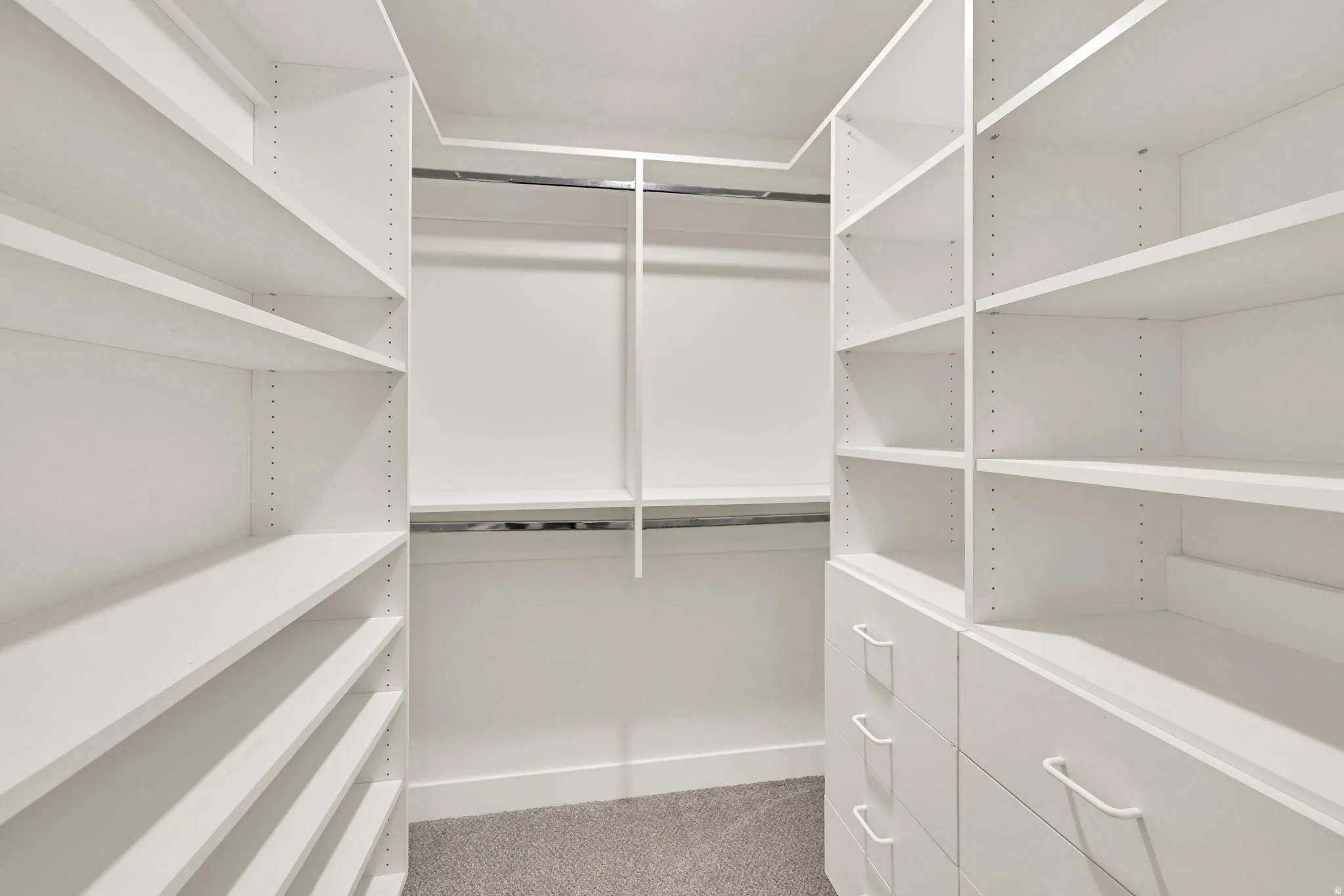 Spacious walk-in closet featuring extensive white shelving and hanging rods, polished concrete flooring, and recessed lighting throughout