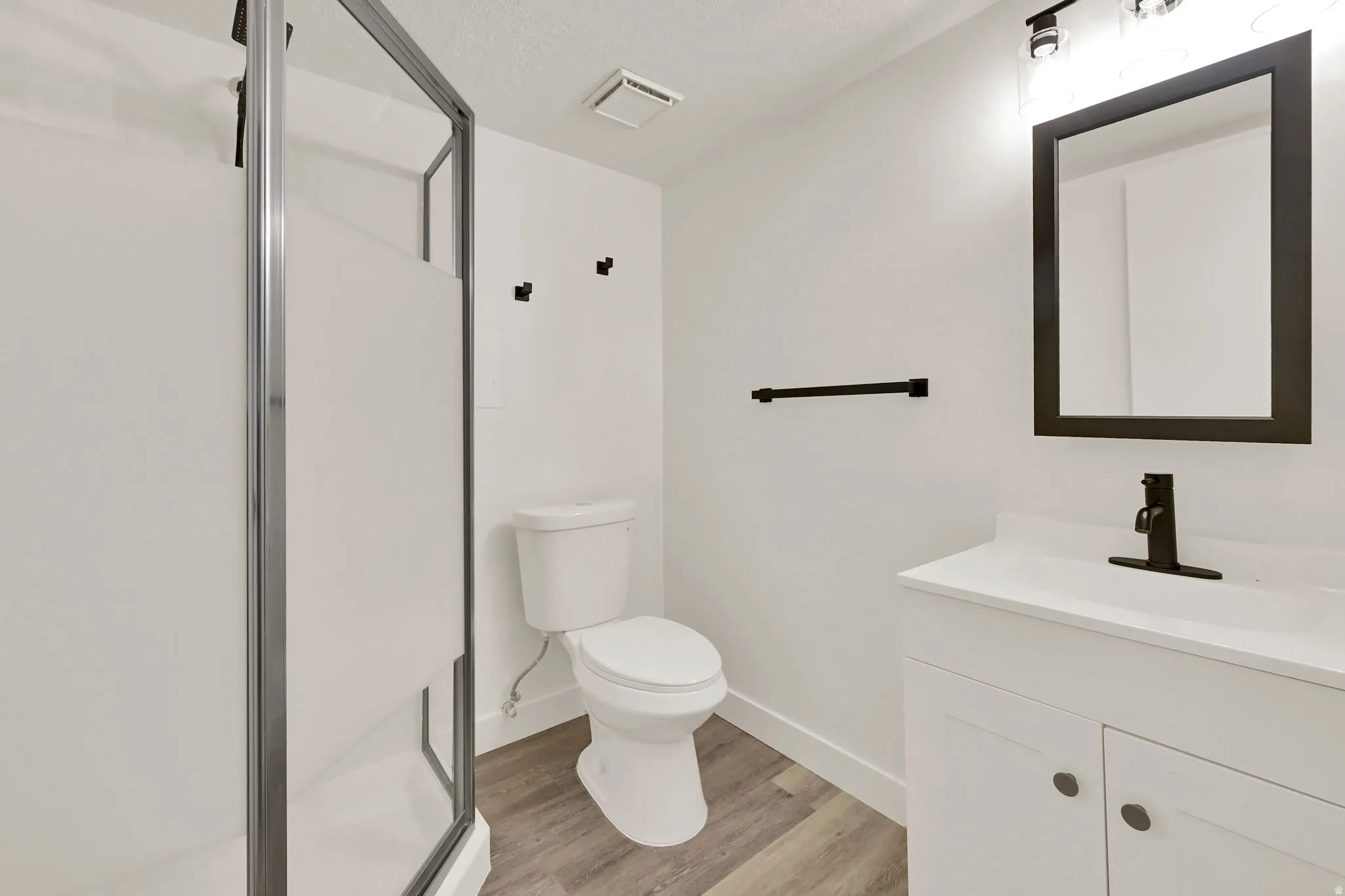 Modern bathroom featuring a single vanity with a white countertop, matte black fixtures, a framed mirror, and a shower with a frosted glass enclosure