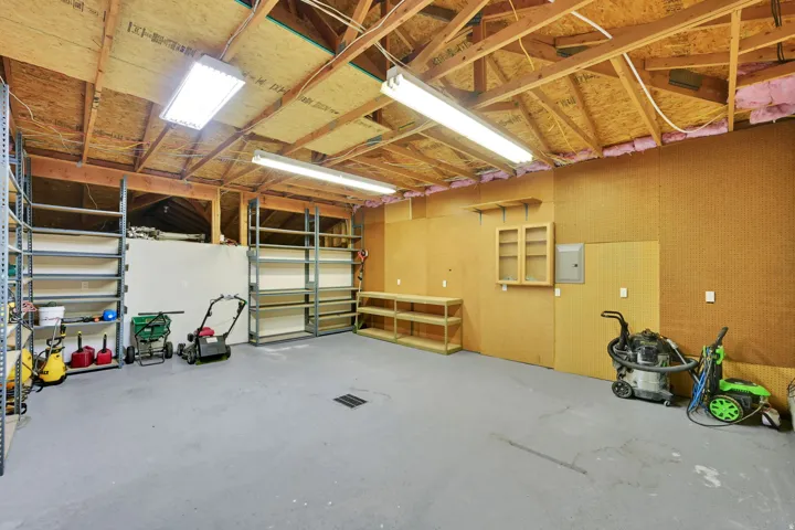 Exposed wood ceiling beams, concrete flooring, overhead fluorescent lighting, built-in shelving, and wall-mounted cabinetry