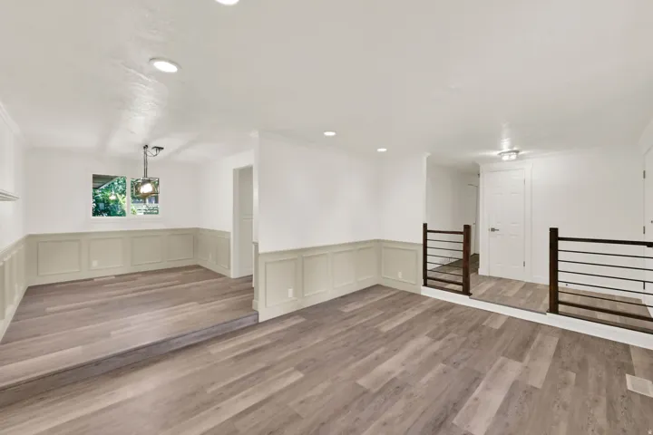 Wood-finish flooring throughout, wainscoting detail, recessed lighting, and a modern horizontal bar railing system