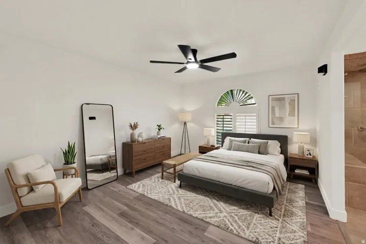 Wood-finish flooring, architectural arched window with plantation shutters, ceiling fan with integrated lighting, recessed shower with neutral tiling, and a frameless glass shower enclosure