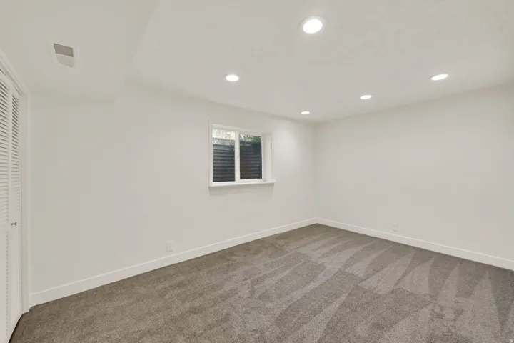 Neutral-toned carpeting, white walls, recessed lighting, and a single window with blinds