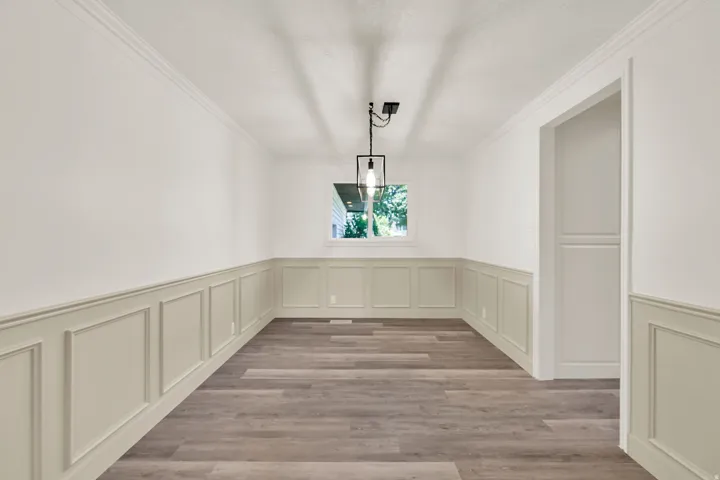 Wood-finish flooring, wainscoting, crown molding, and a modern pendant light fixture