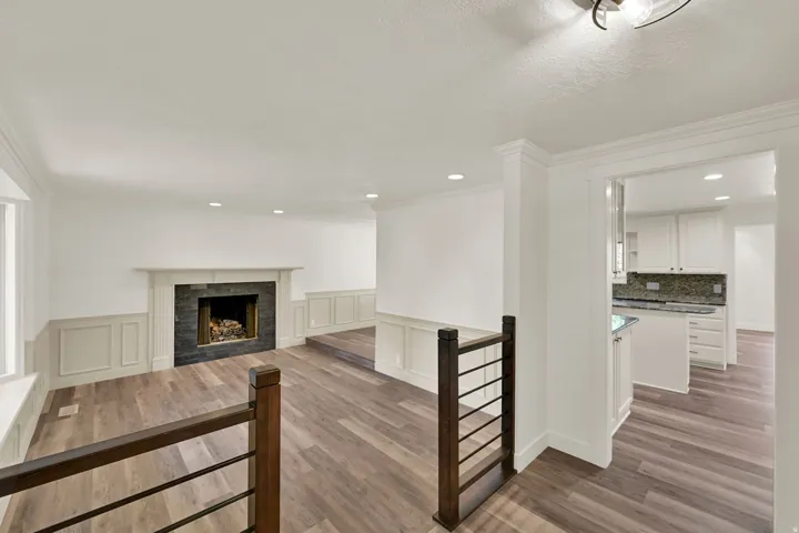 Wood-finish flooring throughout, featuring a fireplace with a dark stone surround and white mantel
