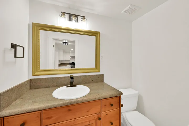 Wood-finish vanity with a drop-in sink, stone countertop, and bronze-finish faucet