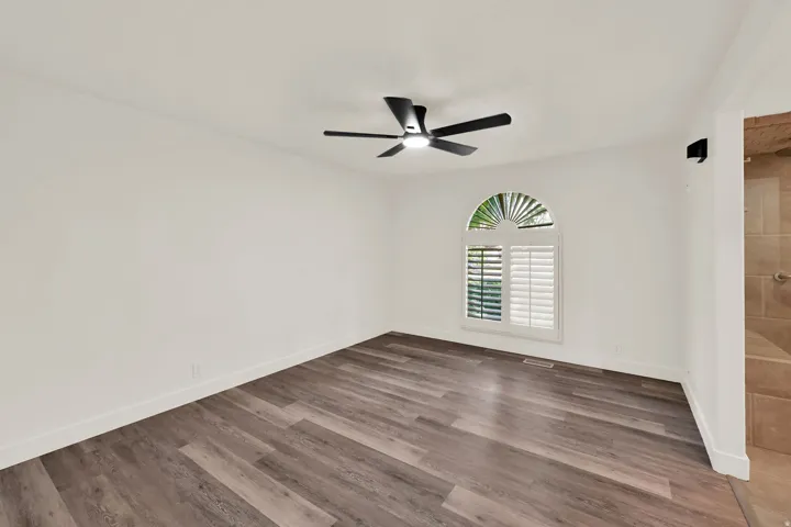 Wood-finish flooring, contemporary ceiling fan, arched window with plantation shutters, recessed lighting, and white walls