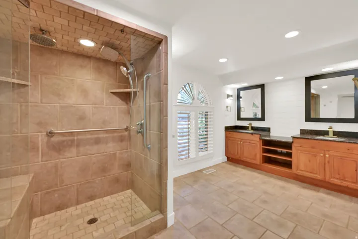 Spa-inspired primary bathroom featuring a spacious walk-in shower with travertine tile surround, rainfall showerhead, and built-in shelving