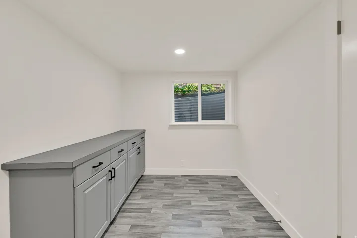Recessed lighting, wood-finish flooring, built-in cabinetry with matte black hardware, solid surface countertop, and a window with white trim
