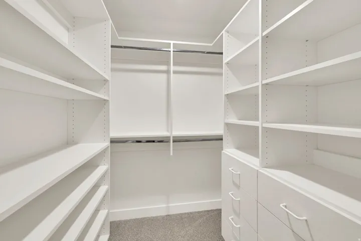 Spacious walk-in closet featuring extensive white shelving and hanging rods, polished concrete flooring, and recessed lighting throughout