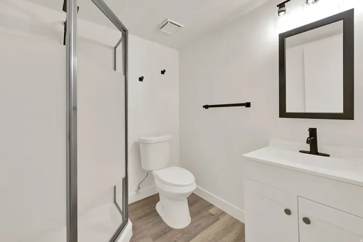 Modern bathroom featuring a single vanity with a white countertop, matte black fixtures, a framed mirror, and a shower with a frosted glass enclosure