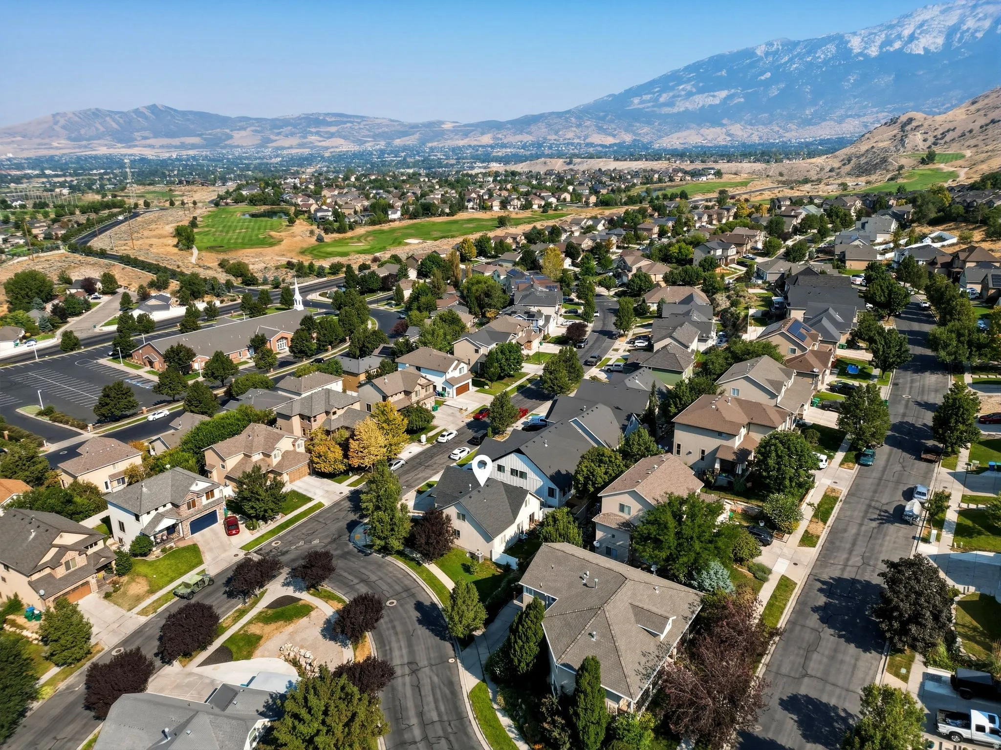 Residential neighborhood with varied rooflines and mature landscaping, surrounded by a natural mountain backdrop and open terrain