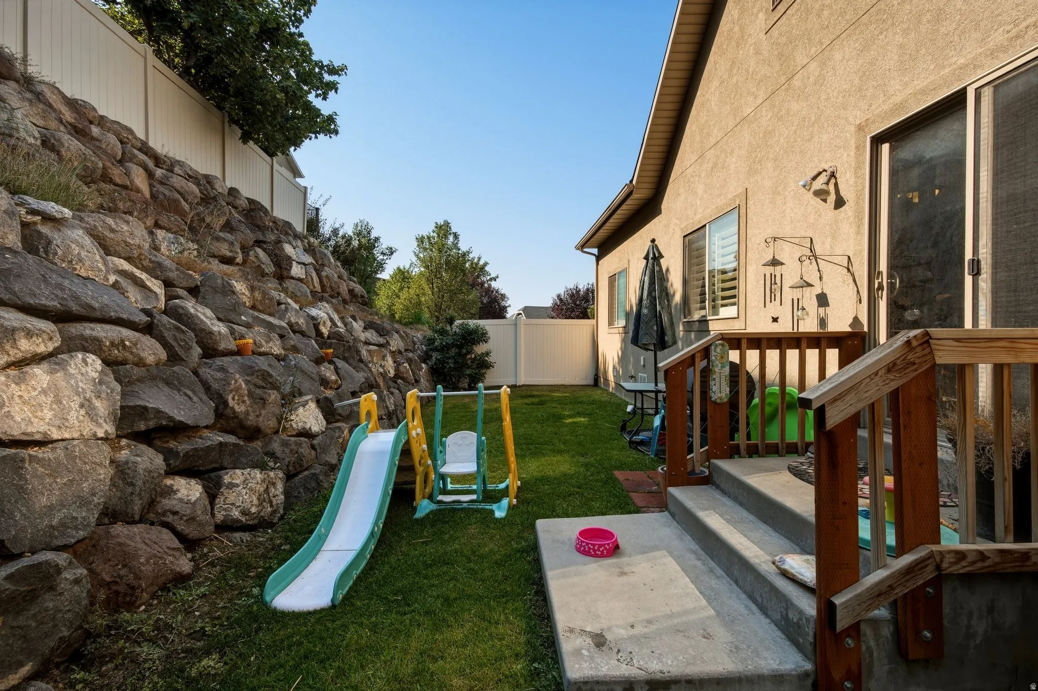 Expansive backyard featuring a stone retaining wall, manicured lawn, and a private rear patio with wood railings