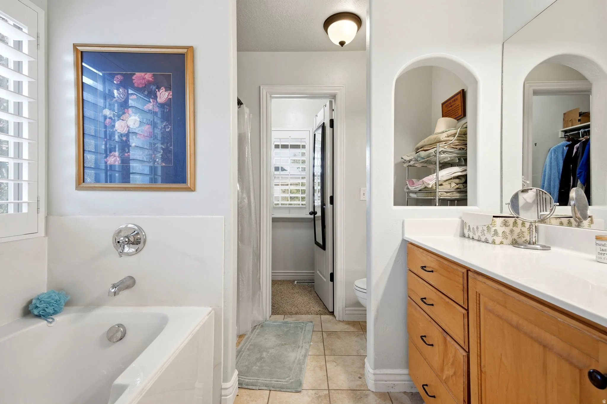 White bathtub with chrome fixtures, wood-finish vanity with white countertop, arched wall niche, and tile flooring