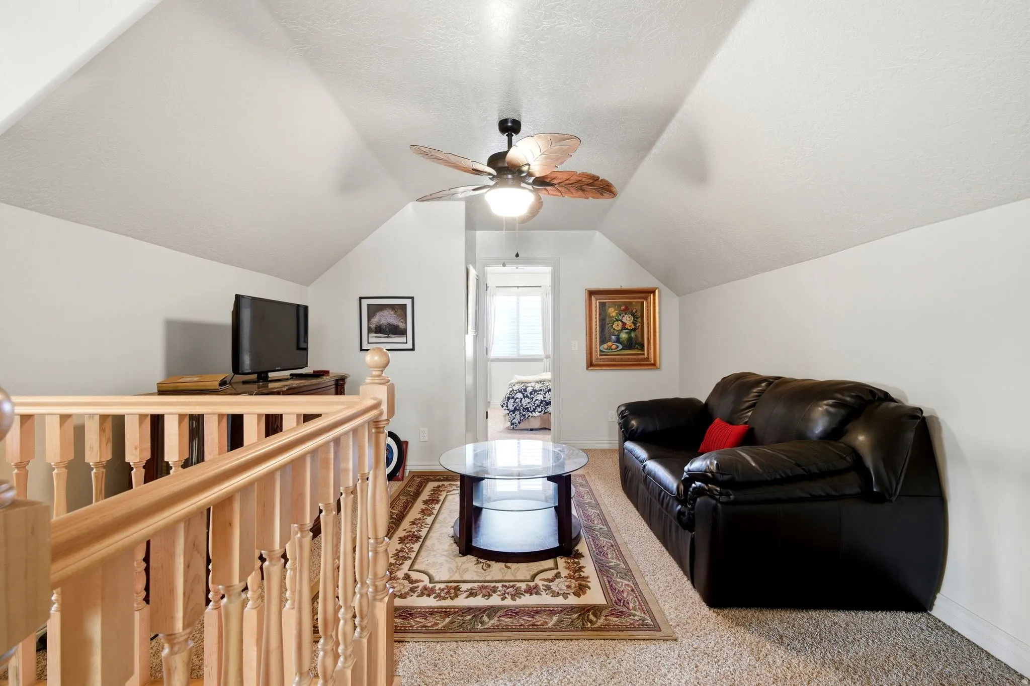 Pitched ceiling with a ceiling fan, carpeted flooring, and a wood balustrade