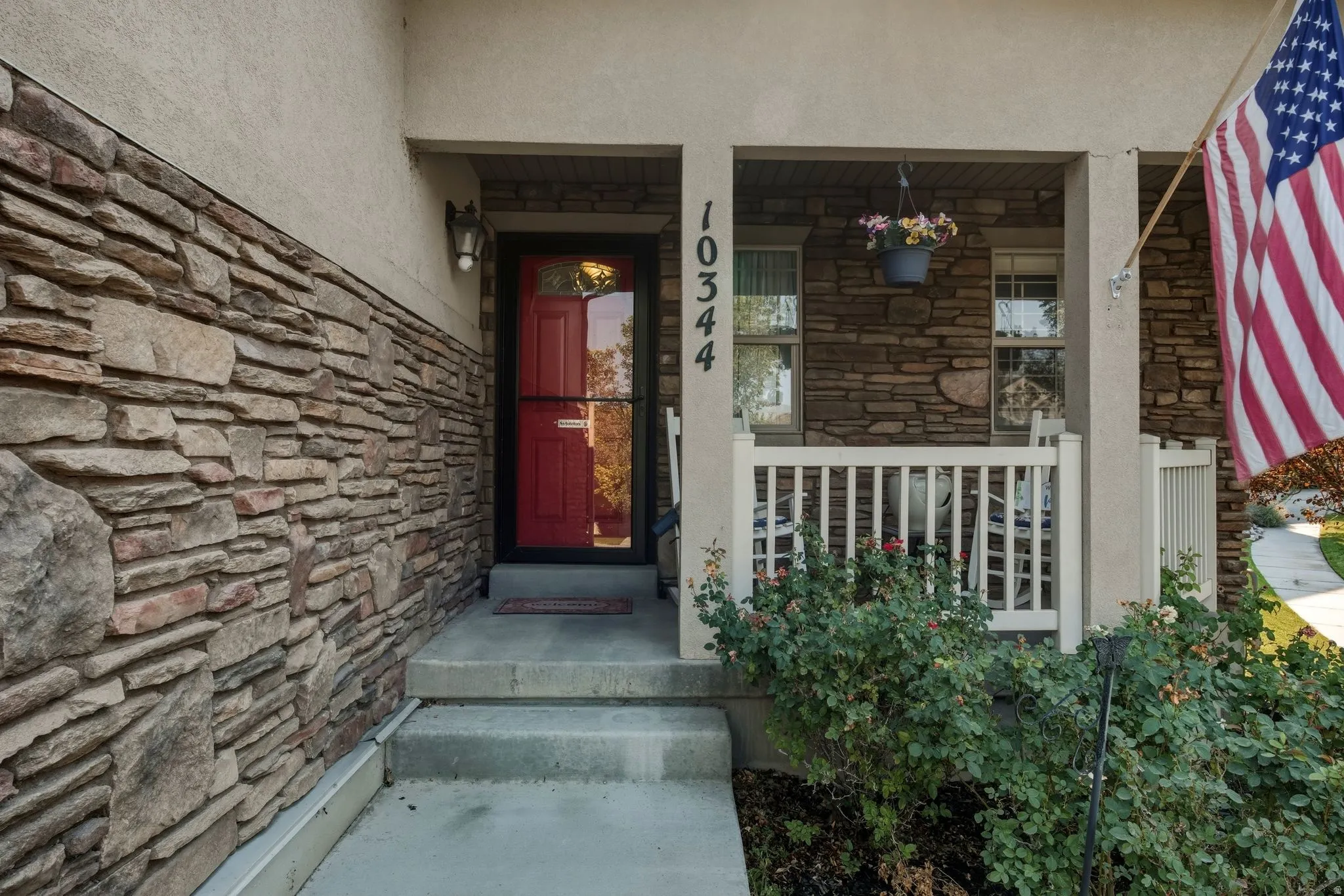 Stone veneer exterior with stucco accents, covered porch, white railing, and a red entry door