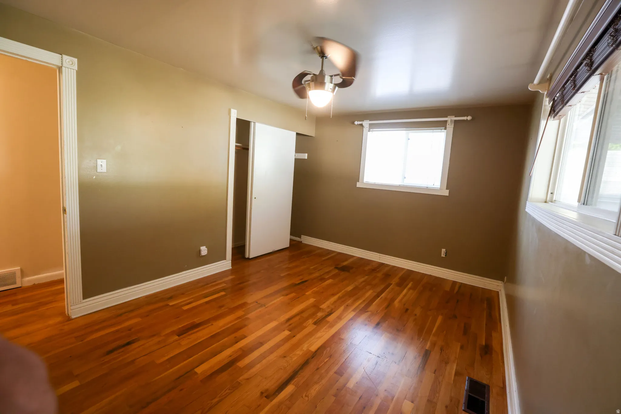 Spacious room featuring rich wood-finish flooring, neutral wall tones, and abundant natural light from multiple windows