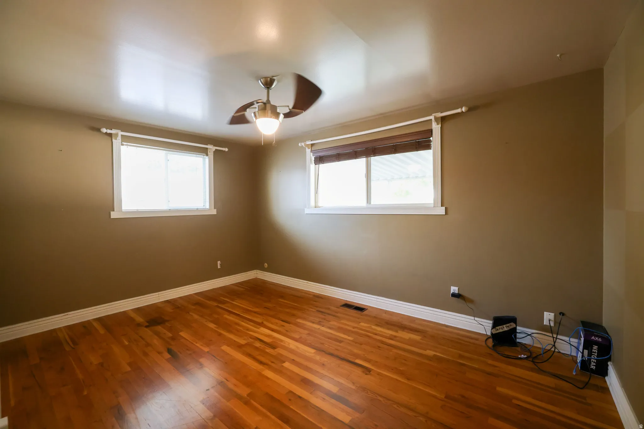 Hardwood flooring, two windows with blinds, ceiling fan with integrated lighting, and neutral wall paint