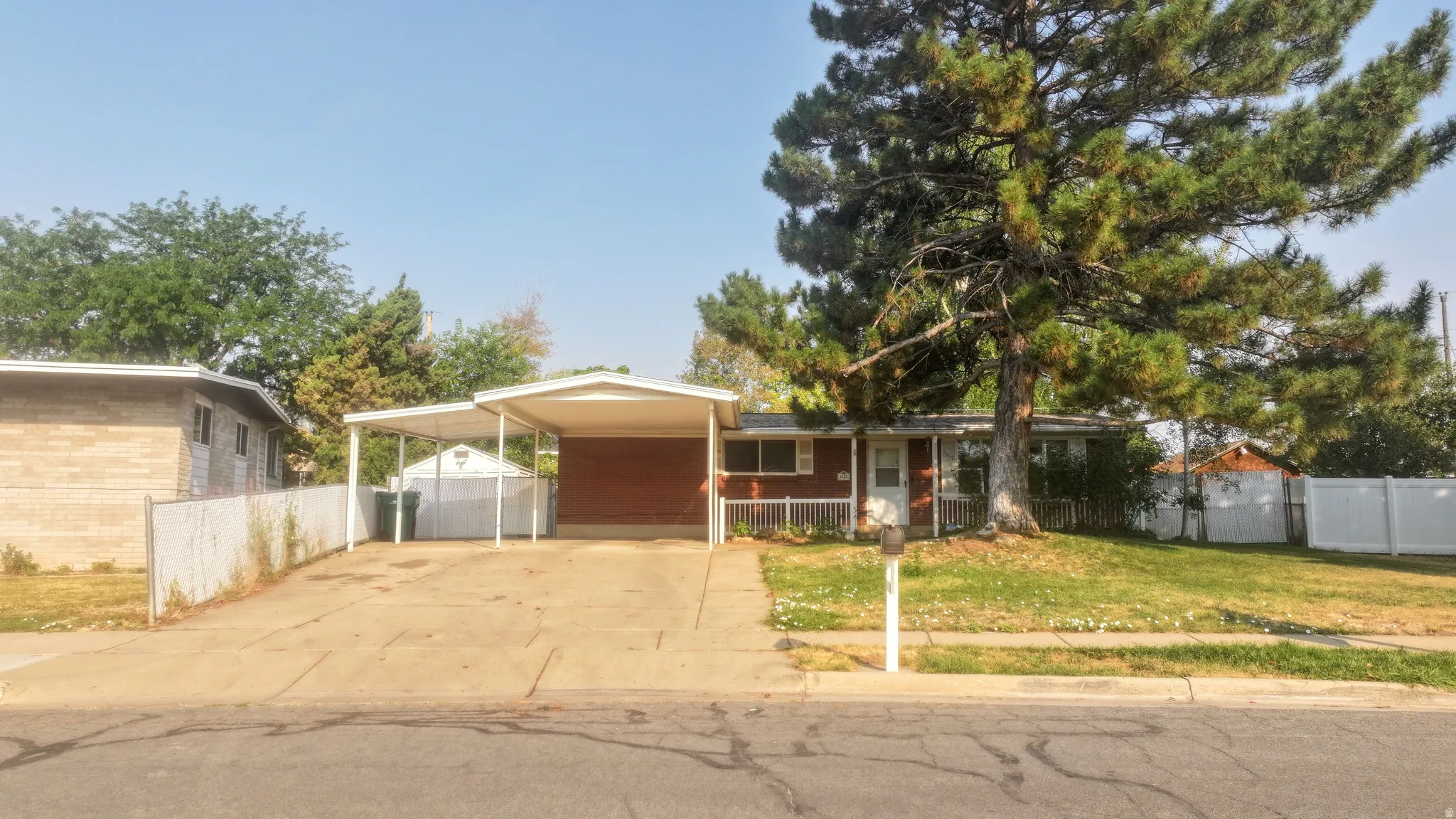 Brick exterior with white trim, two-car carport, concrete driveway, and mature front yard tree