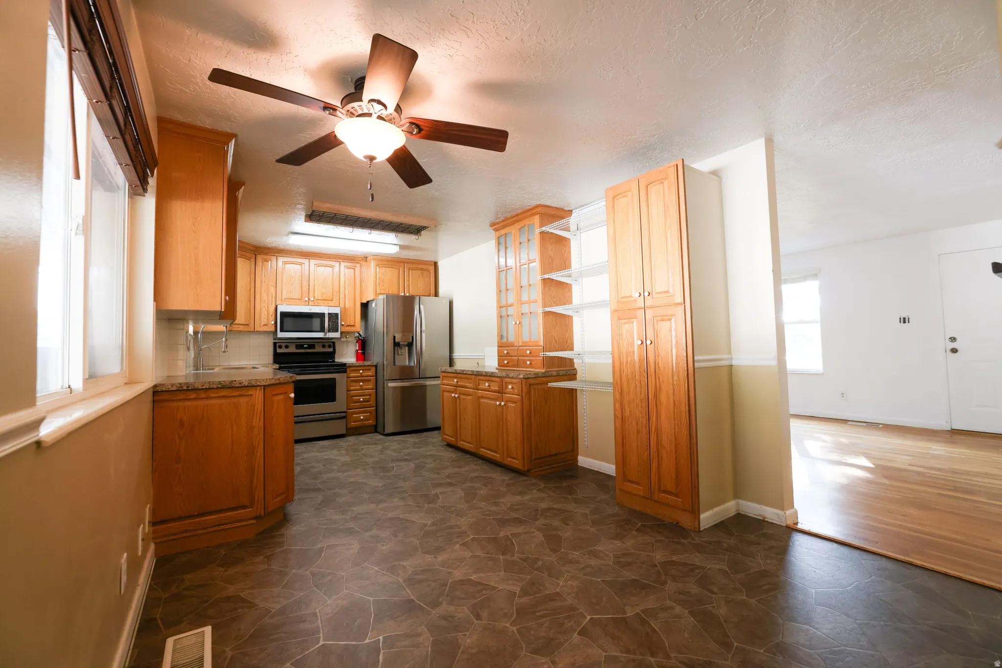 Kitchen featuring wood-finish cabinetry, stainless steel appliances, a ceiling fan, and stone-look flooring