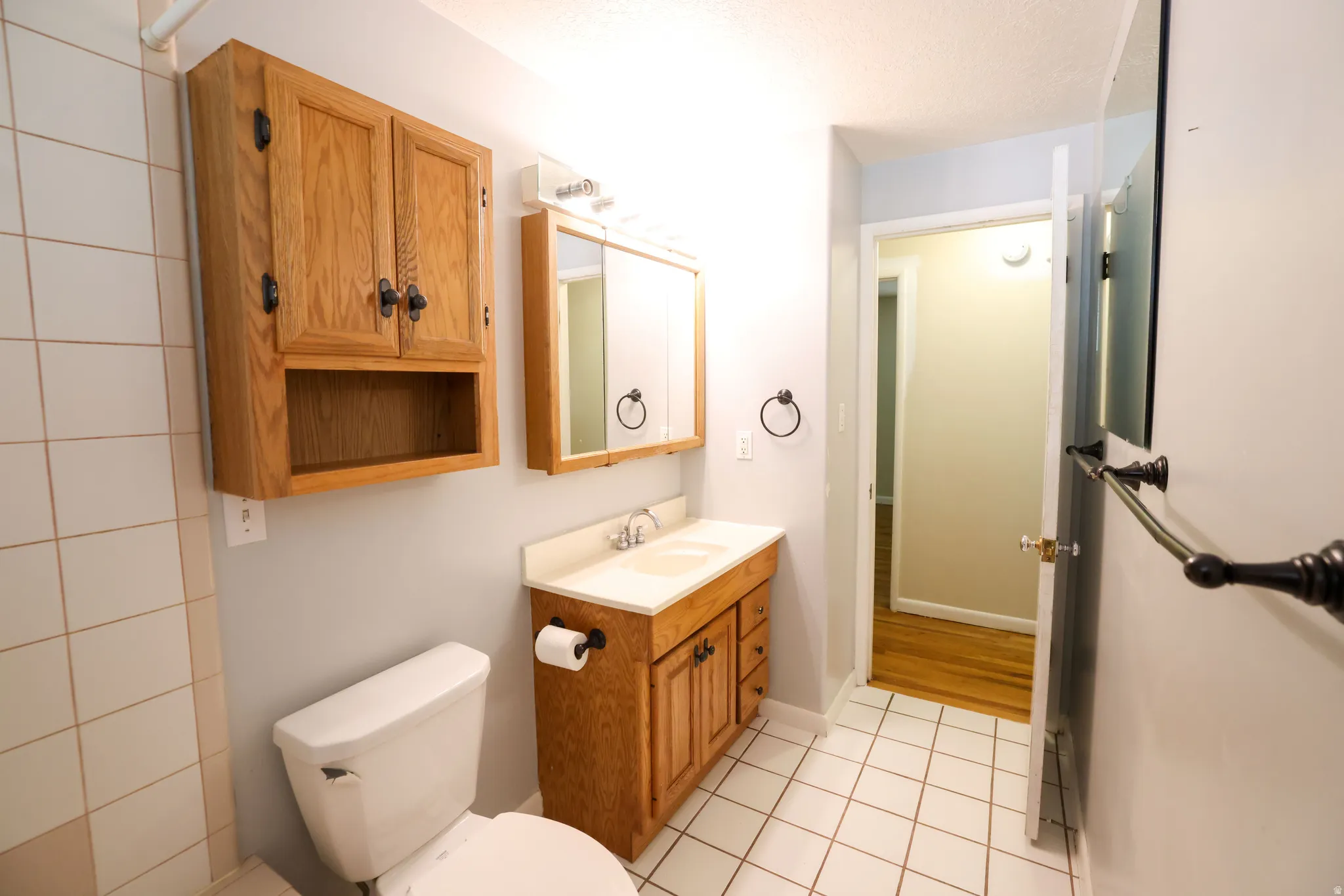 Bathroom featuring tile flooring, a wood-finish vanity with an integrated sink, a wall-mounted wood-finish cabinet, and a mirrored medicine cabinet
