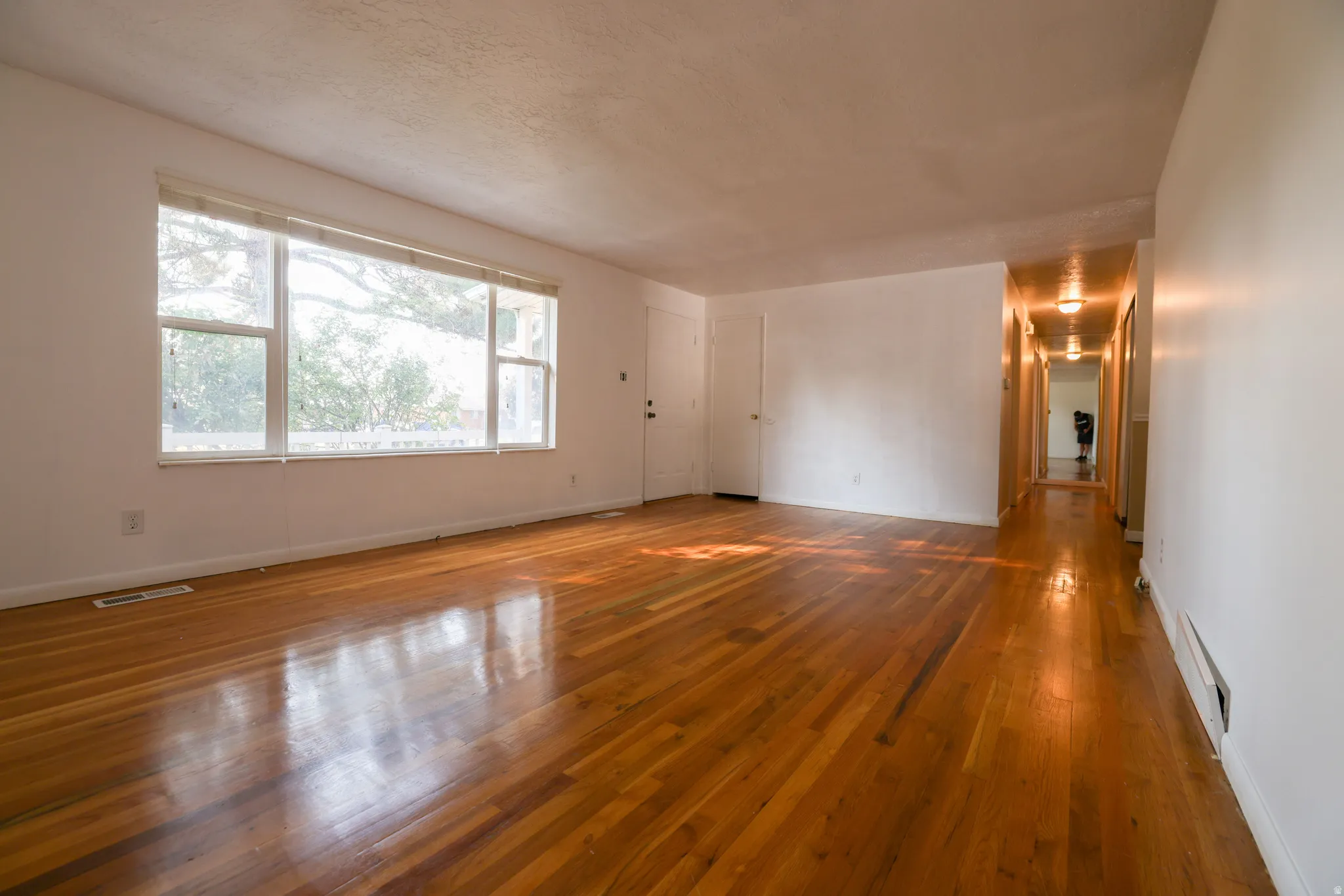 Spacious living area showcasing rich wood-finish flooring and abundant natural light