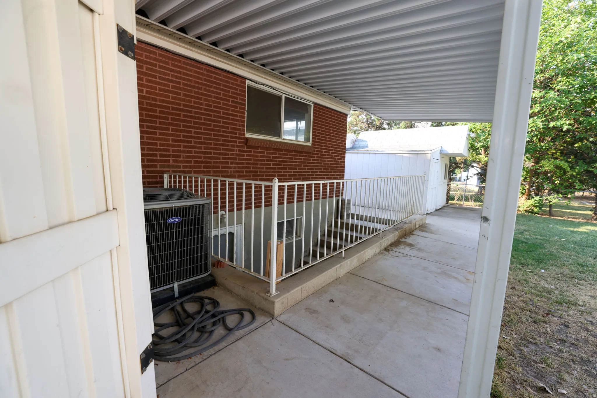 Red brick exterior, concrete patio, white metal railing, corrugated metal patio cover, exterior HVAC unit