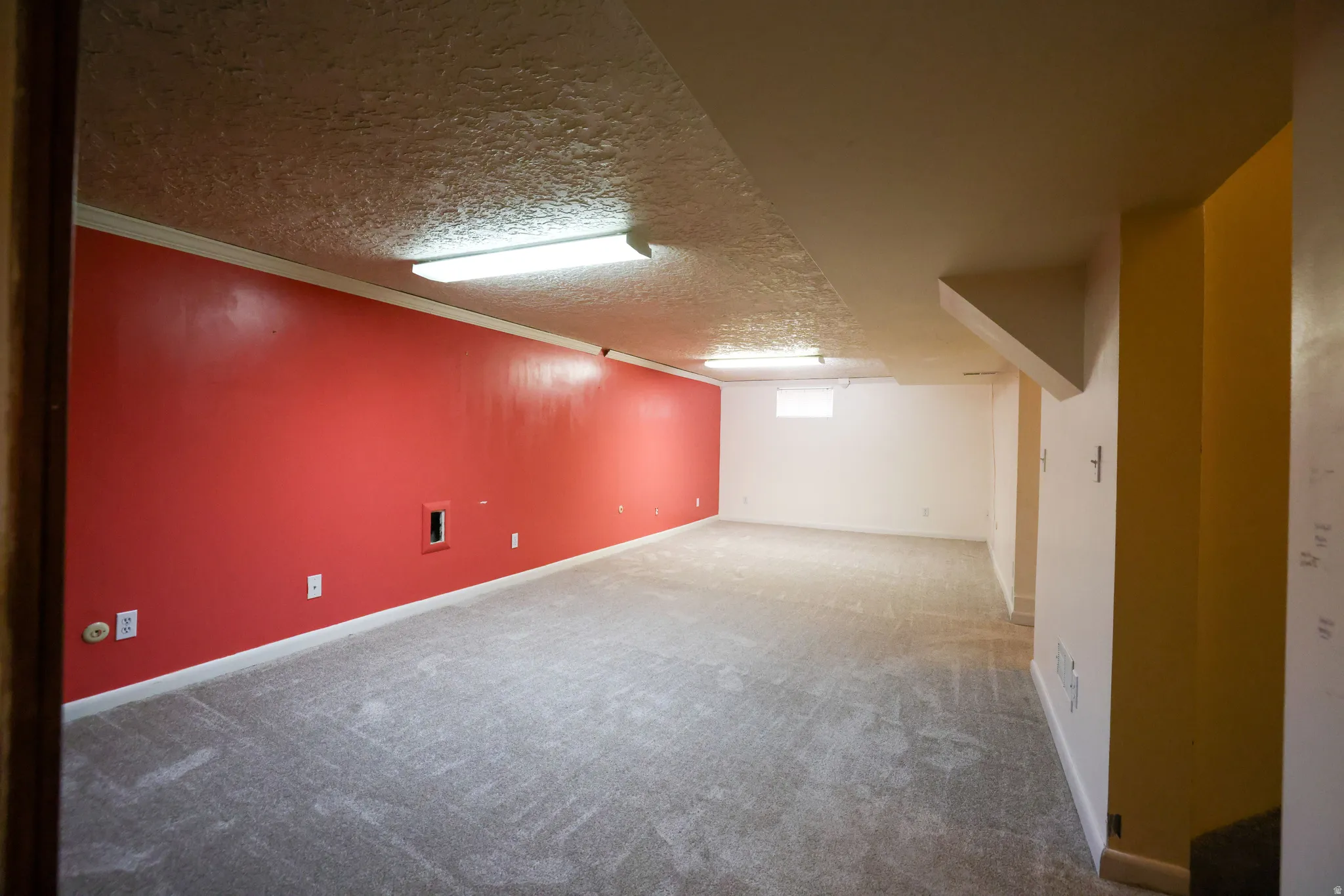 Spacious room featuring carpeting, multiple electrical outlets, overhead fluorescent lighting, and a small window