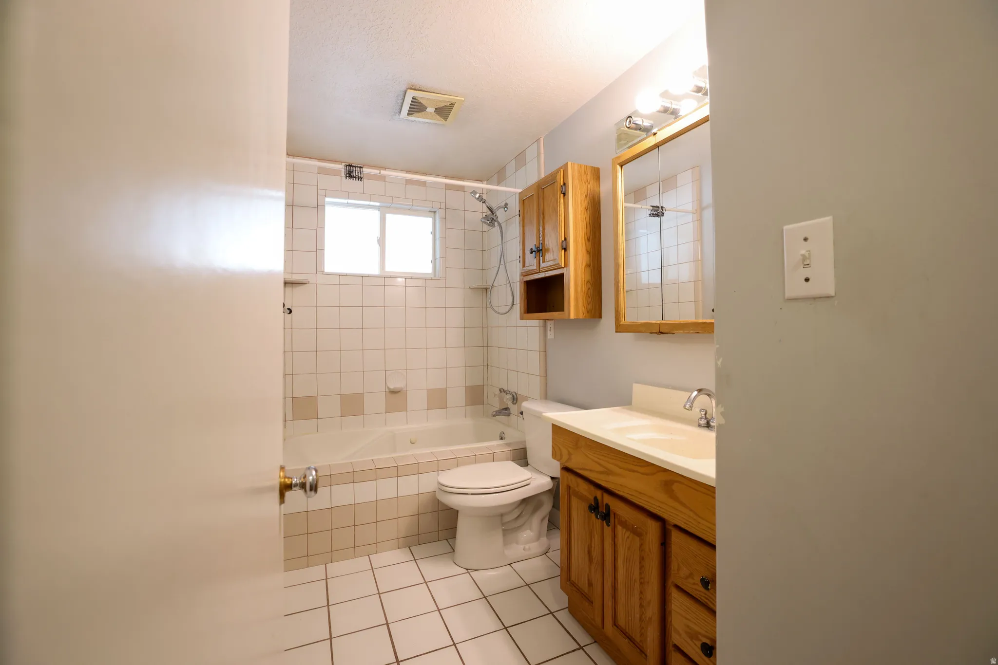 Bathroom featuring a built-in tub with tile surround, a single window, and a wood-finish vanity with an integrated sink